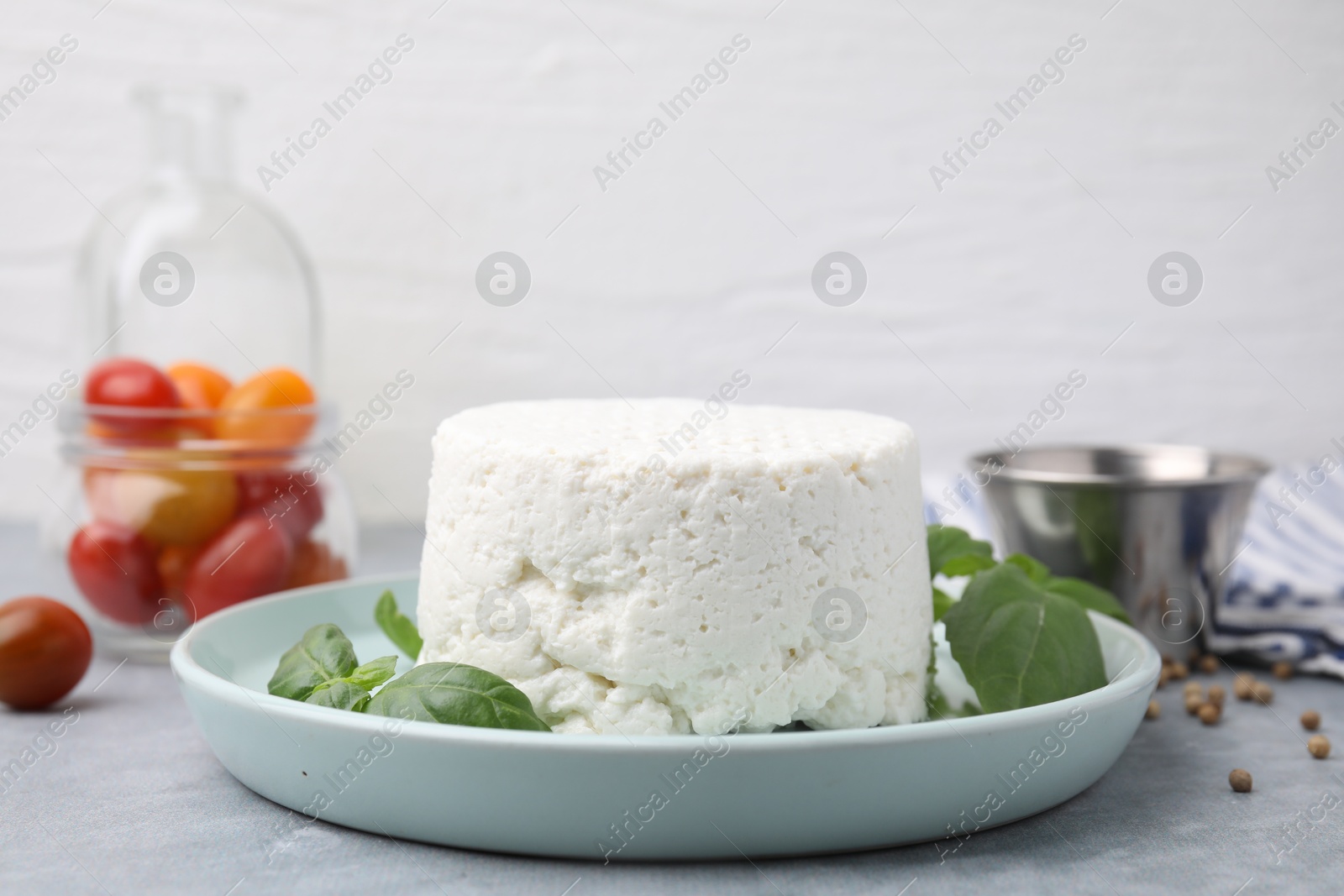 Photo of Fresh ricotta (cream cheese) and basil on gray table, closeup