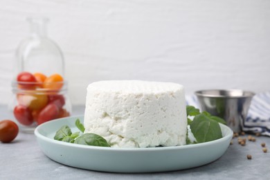 Fresh ricotta (cream cheese) and basil on gray table, closeup