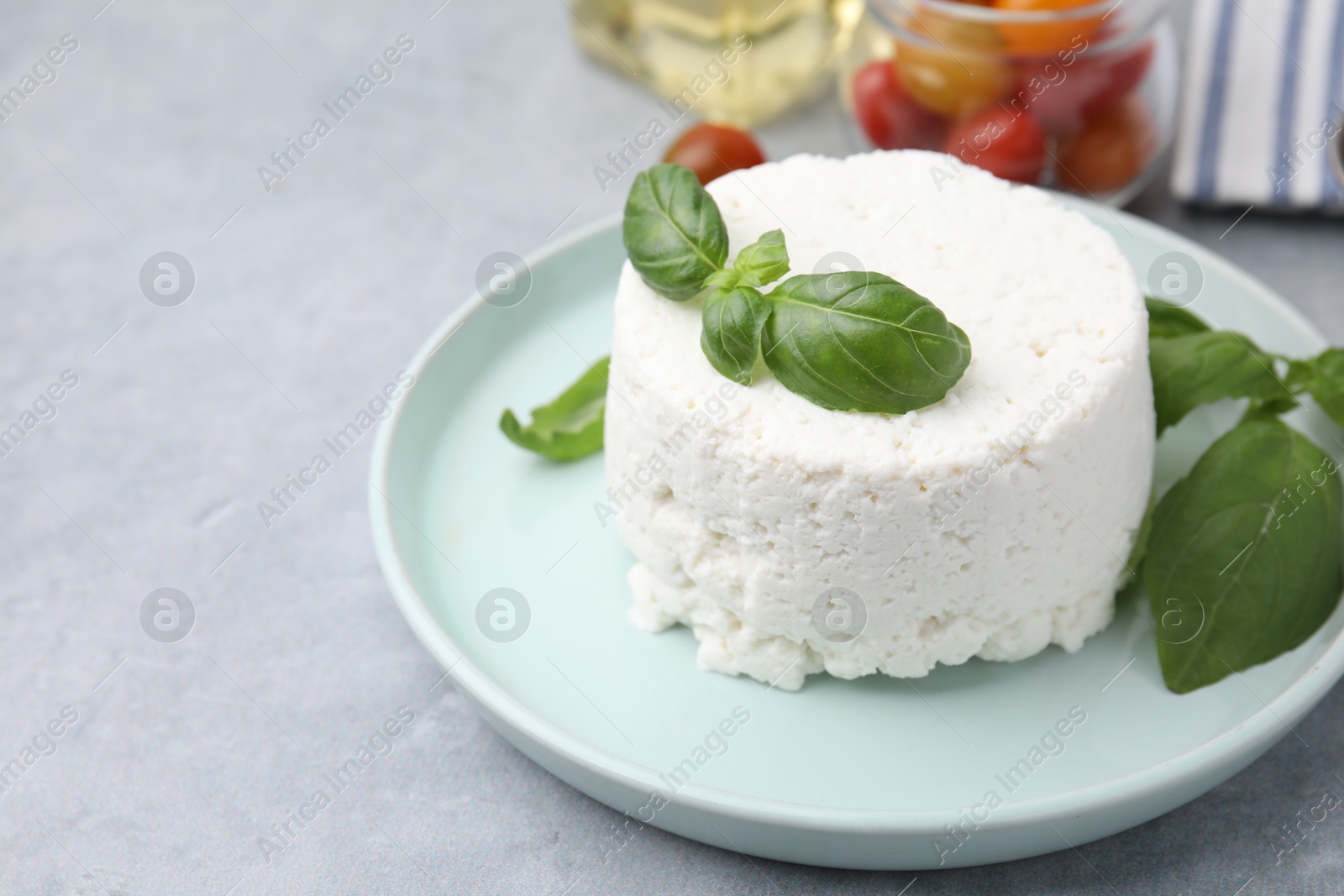 Photo of Fresh ricotta (cream cheese) and basil on gray table, closeup. Space for text