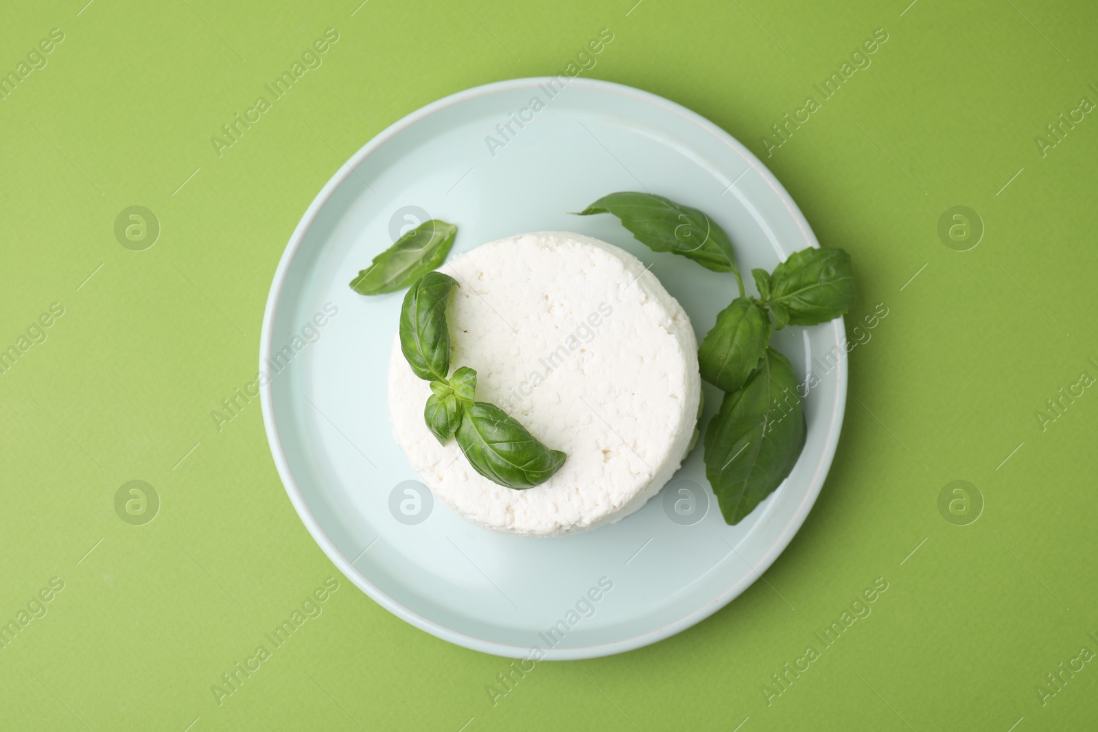 Photo of Fresh ricotta (cream cheese) and basil on green table, top view