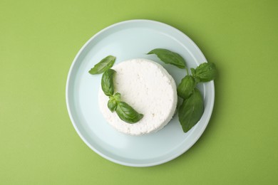 Fresh ricotta (cream cheese) and basil on green table, top view