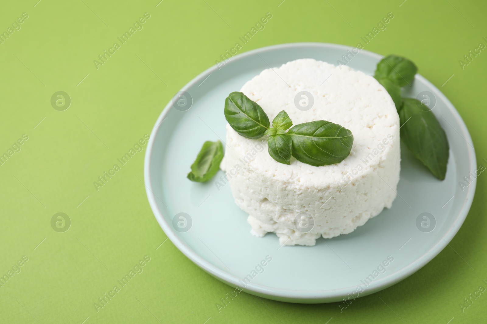 Photo of Fresh ricotta (cream cheese) and basil on green table. Space for text