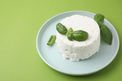 Photo of Fresh ricotta (cream cheese) and basil on green table. Space for text