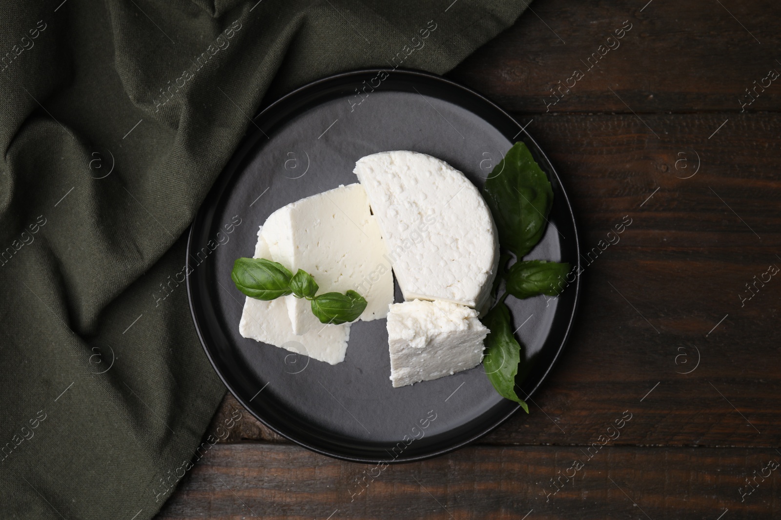 Photo of Fresh ricotta (cream cheese) and basil on wooden table, top view