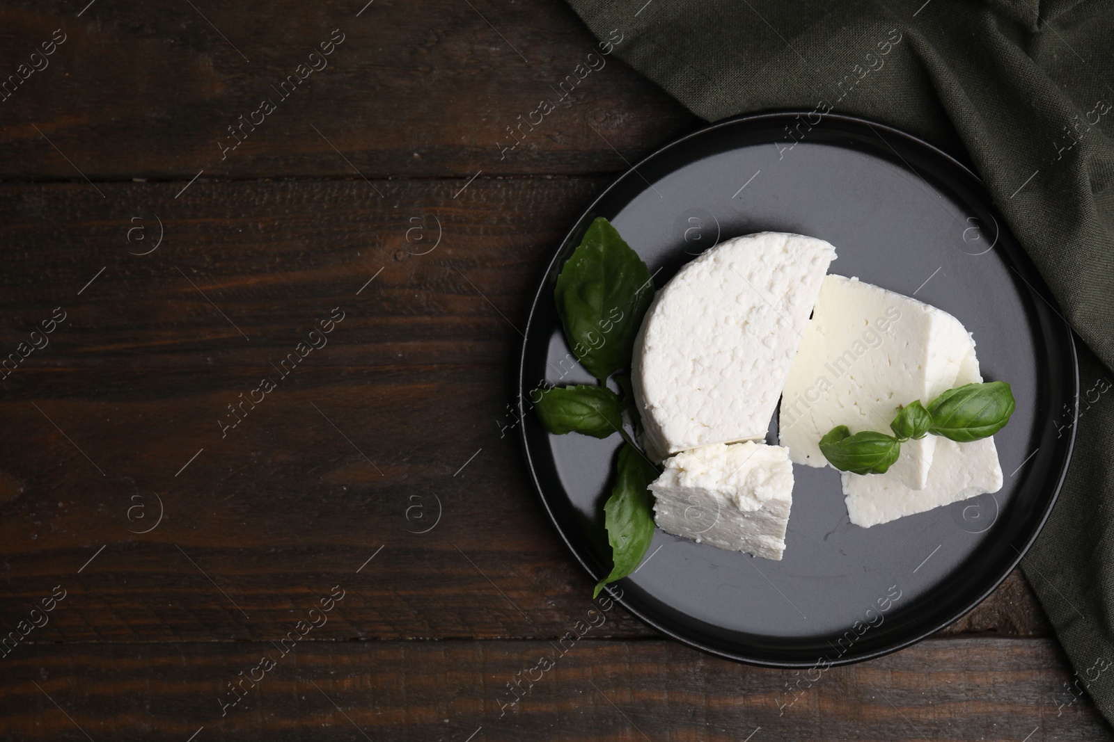 Photo of Fresh ricotta (cream cheese) and basil on wooden table, top view. Space for text