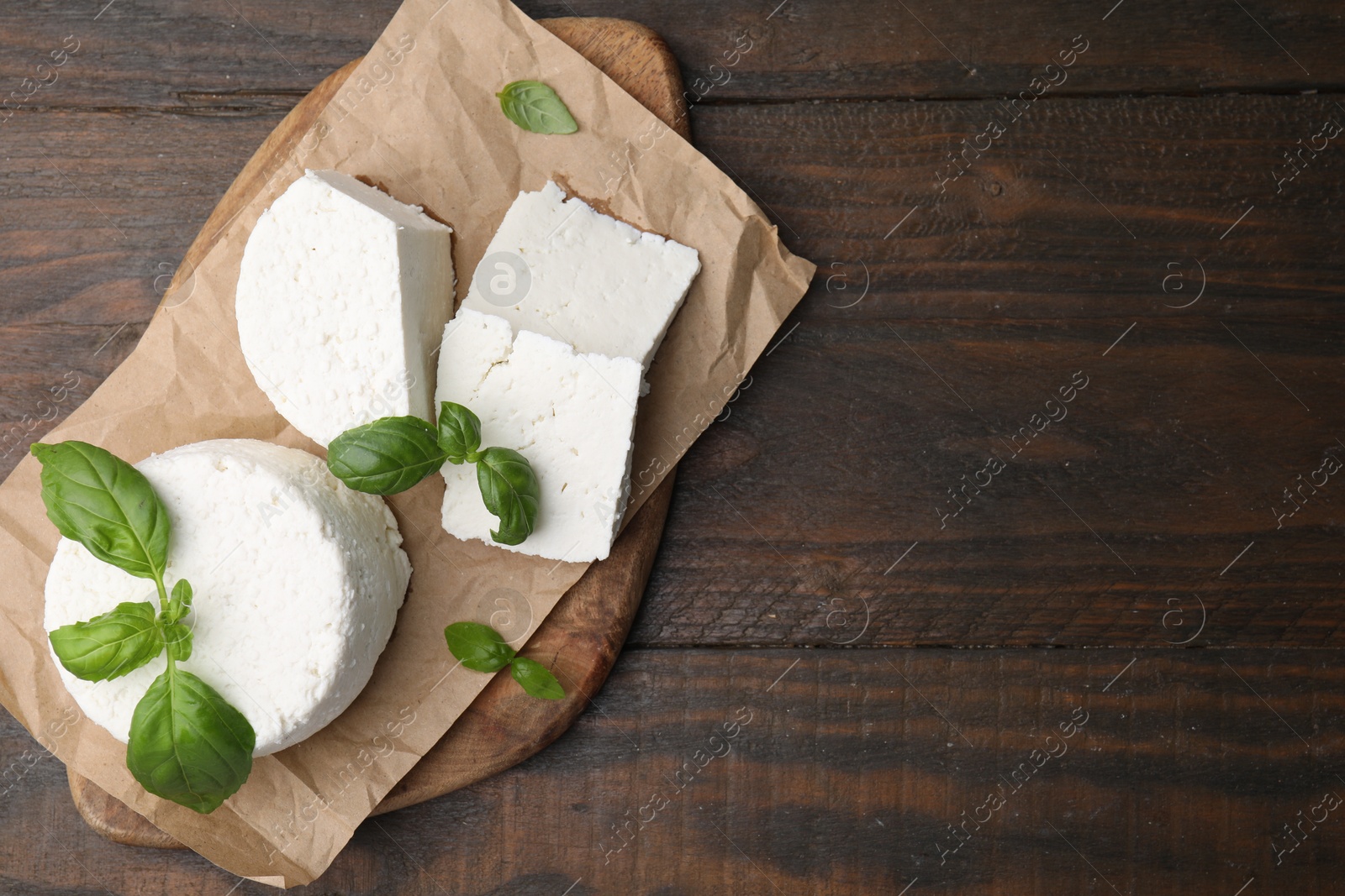 Photo of Fresh ricotta (cream cheese) and basil on wooden table, top view. Space for text