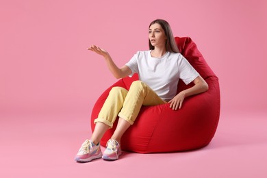 Photo of Emotional woman sitting on red bean bag chair against pink background