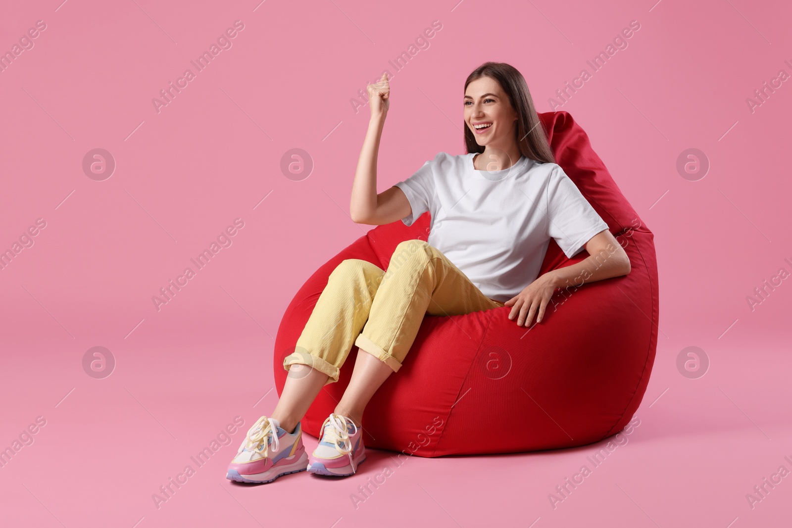 Photo of Smiling woman sitting on red bean bag chair against pink background