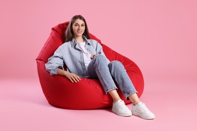 Photo of Smiling woman sitting on red bean bag chair against pink background