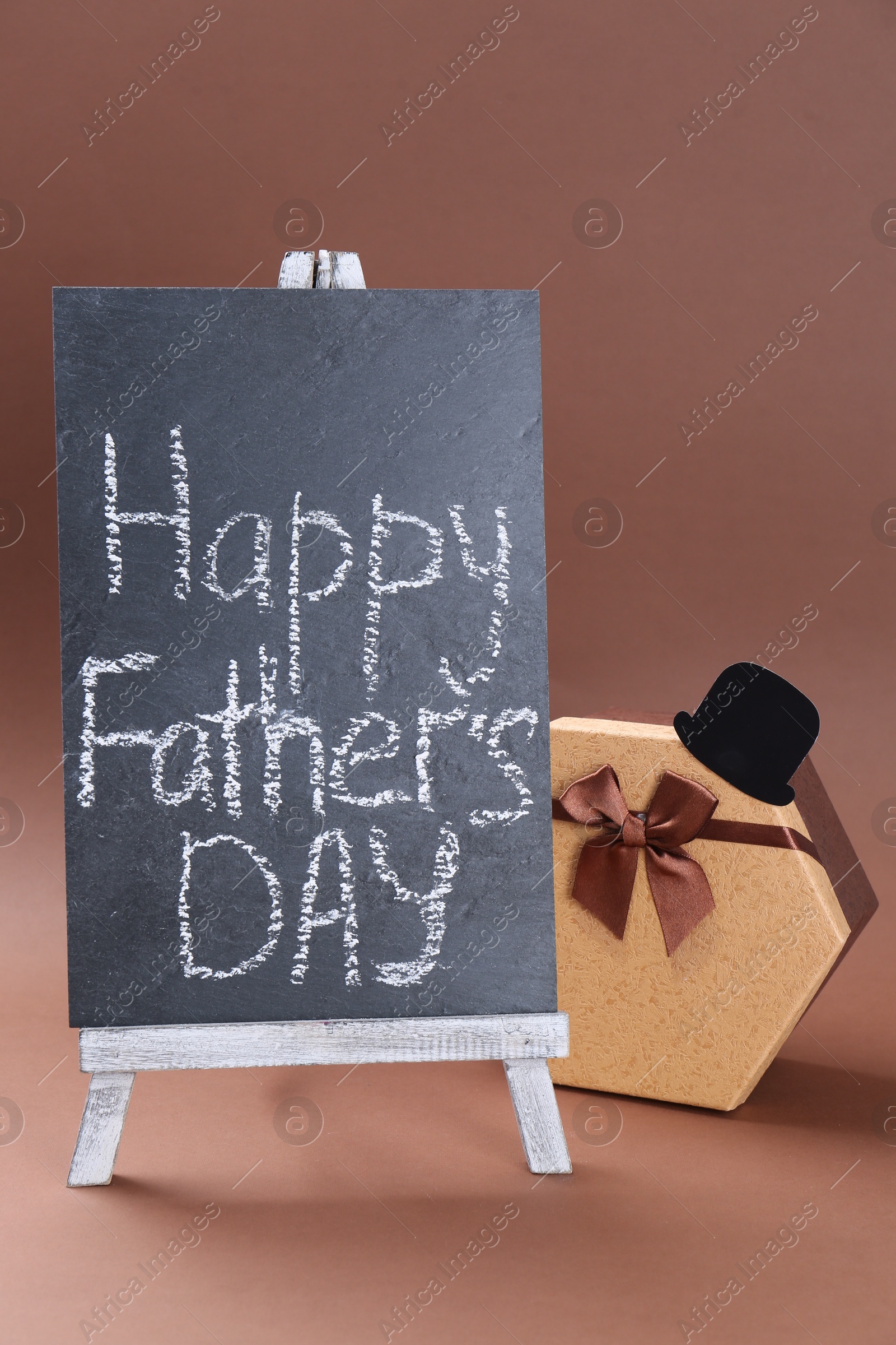 Photo of Mini easel with phrase Happy Father's Day, hat and gift box on light brown background