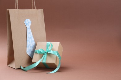 Photo of Happy Father's Day. Paper bag with tie and gift box on light brown background, space for text