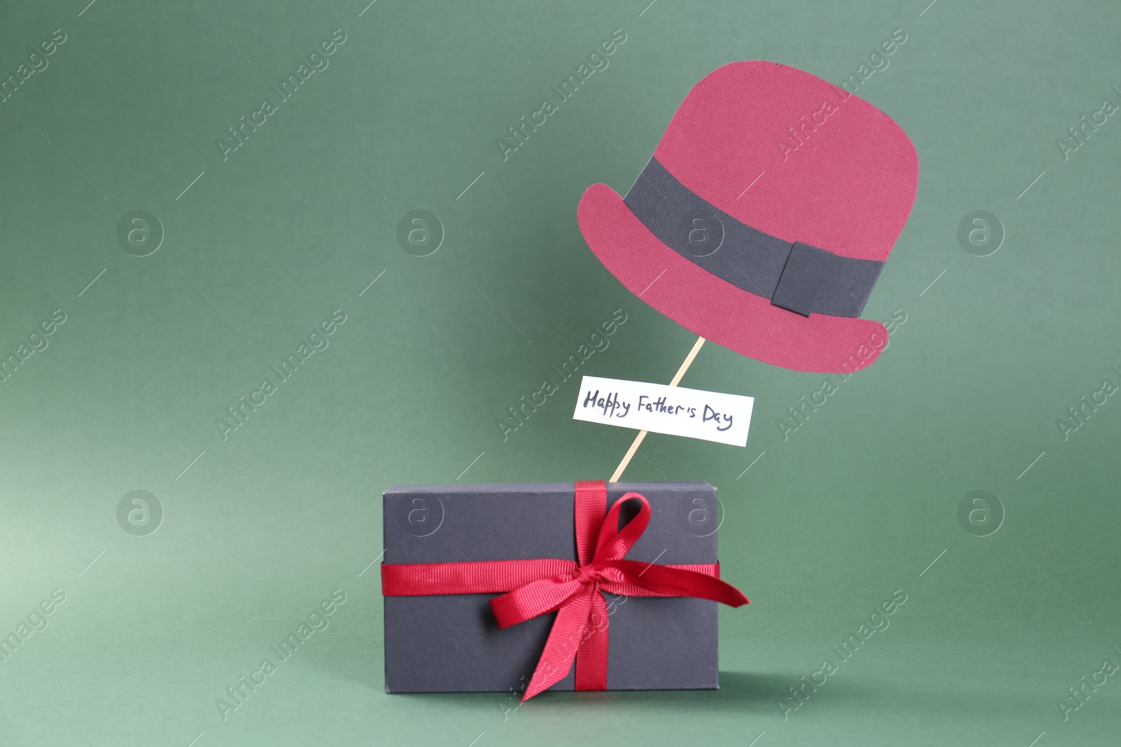 Photo of Phrase Happy Father's Day, gift box and paper hat on green background