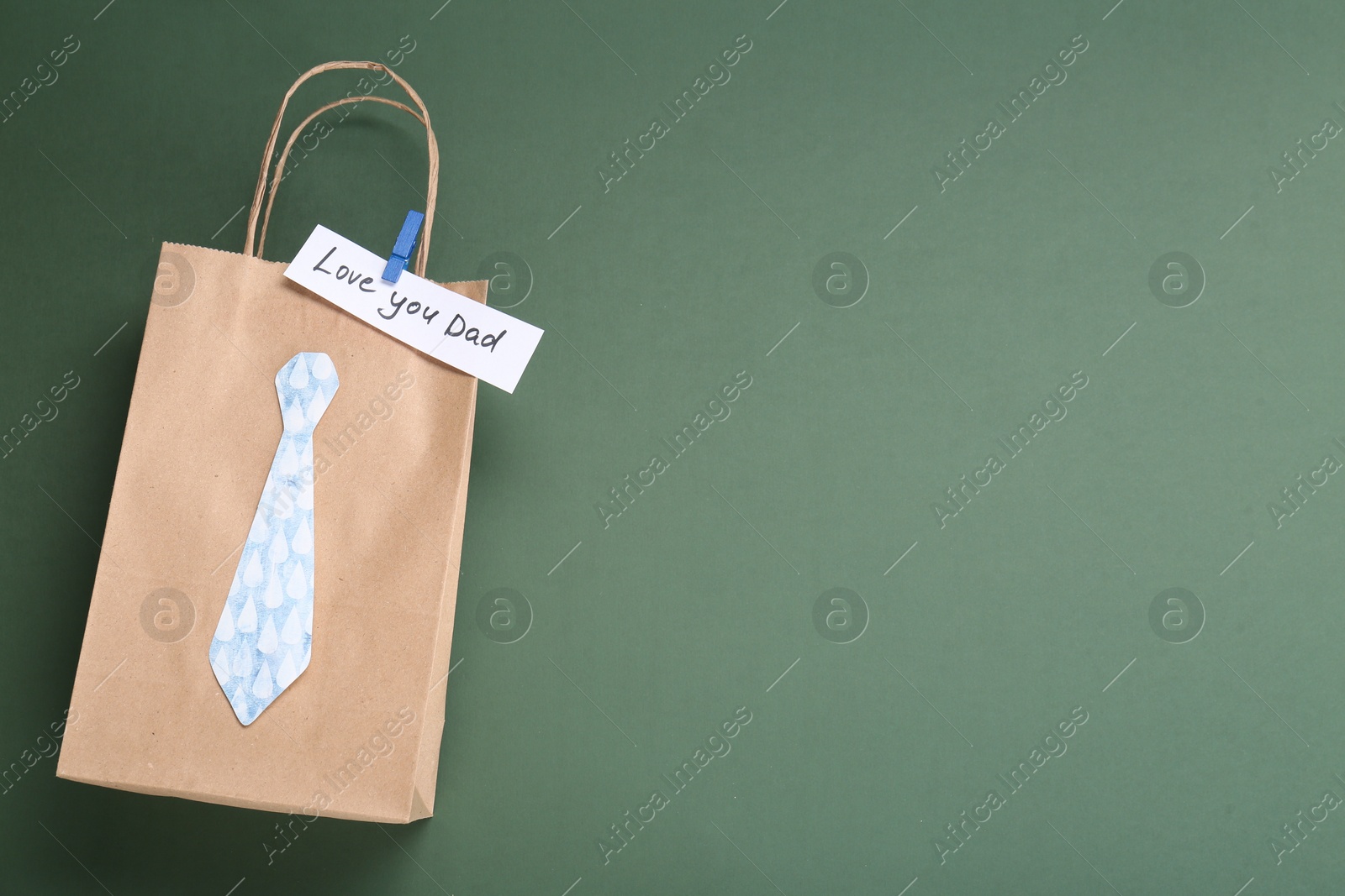 Photo of Happy Father's Day. Paper bag with tie and phrase Love You Dad on green background, top view. Space for text