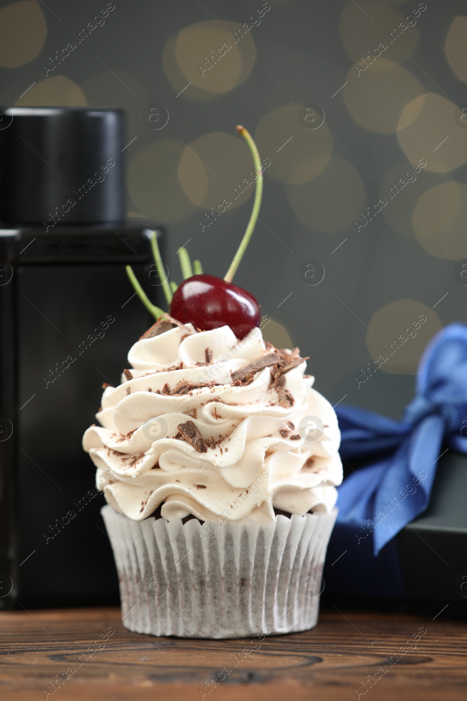 Photo of Happy Father's Day. Cupcake, gift box and perfume on wooden table against blurred lights, closeup