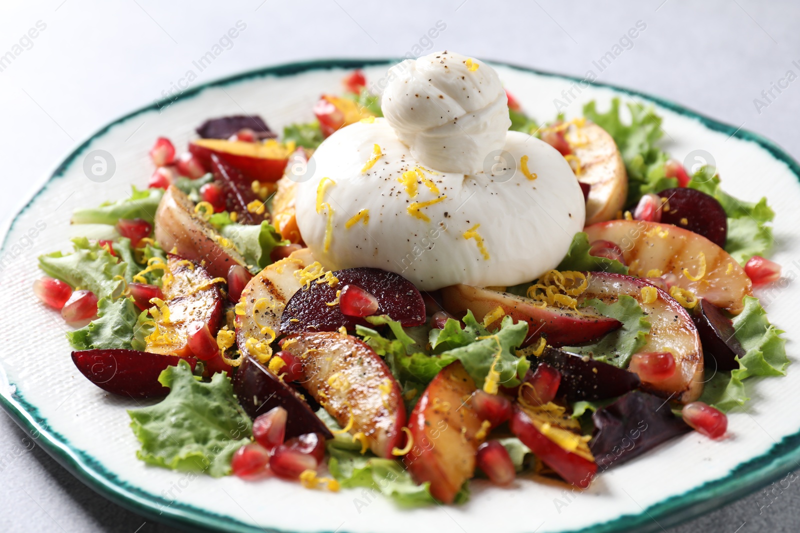 Photo of Plate with fresh burrata salad on grey table, closeup