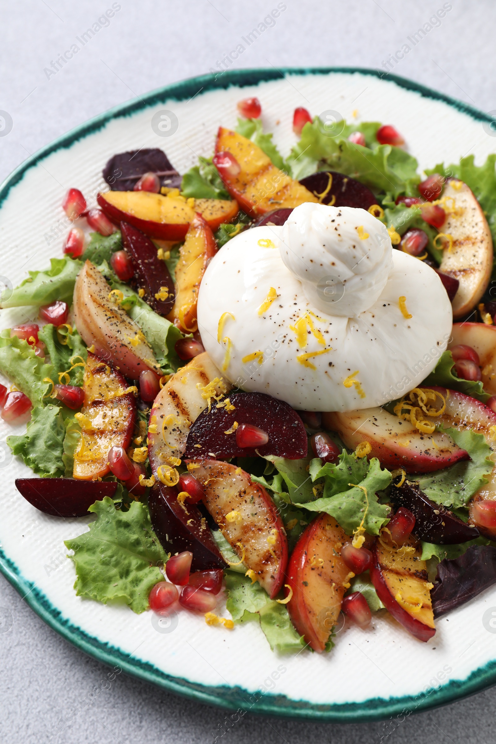 Photo of Plate with fresh burrata salad on grey table, closeup