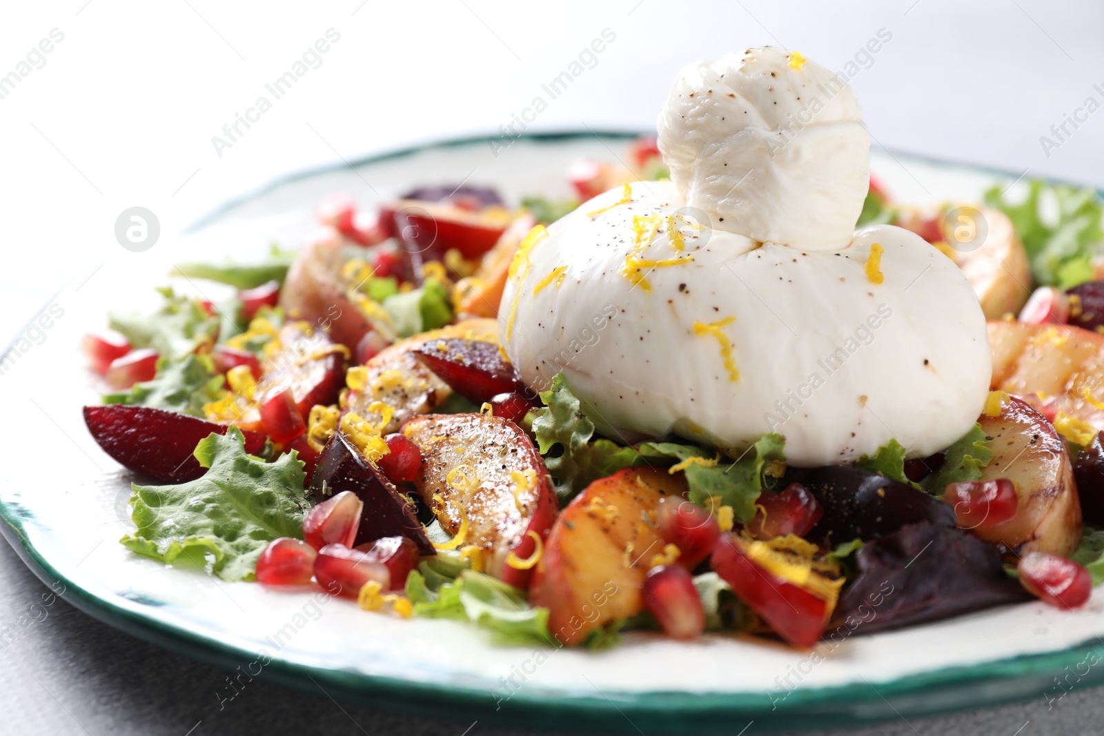 Photo of Plate with fresh burrata salad on grey table, closeup