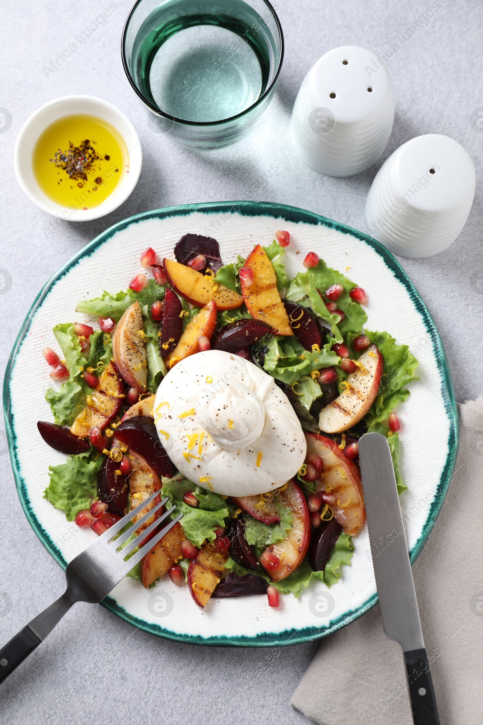 Photo of Plate with fresh burrata salad served on grey textured table, flat lay