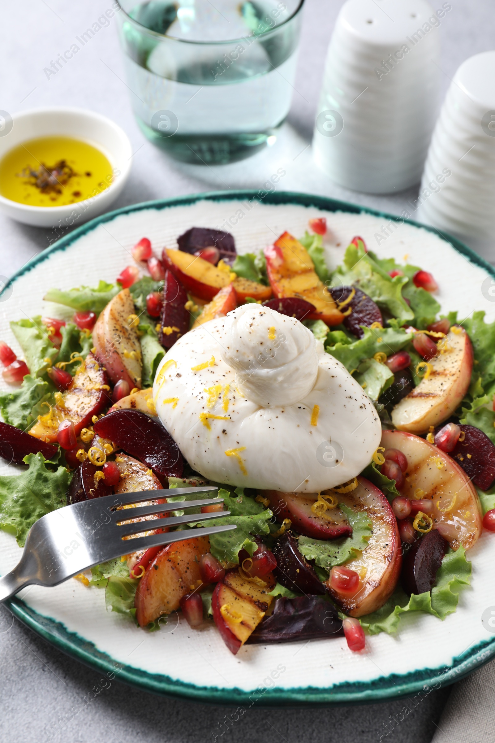 Photo of Plate with fresh burrata salad on grey textured table, closeup