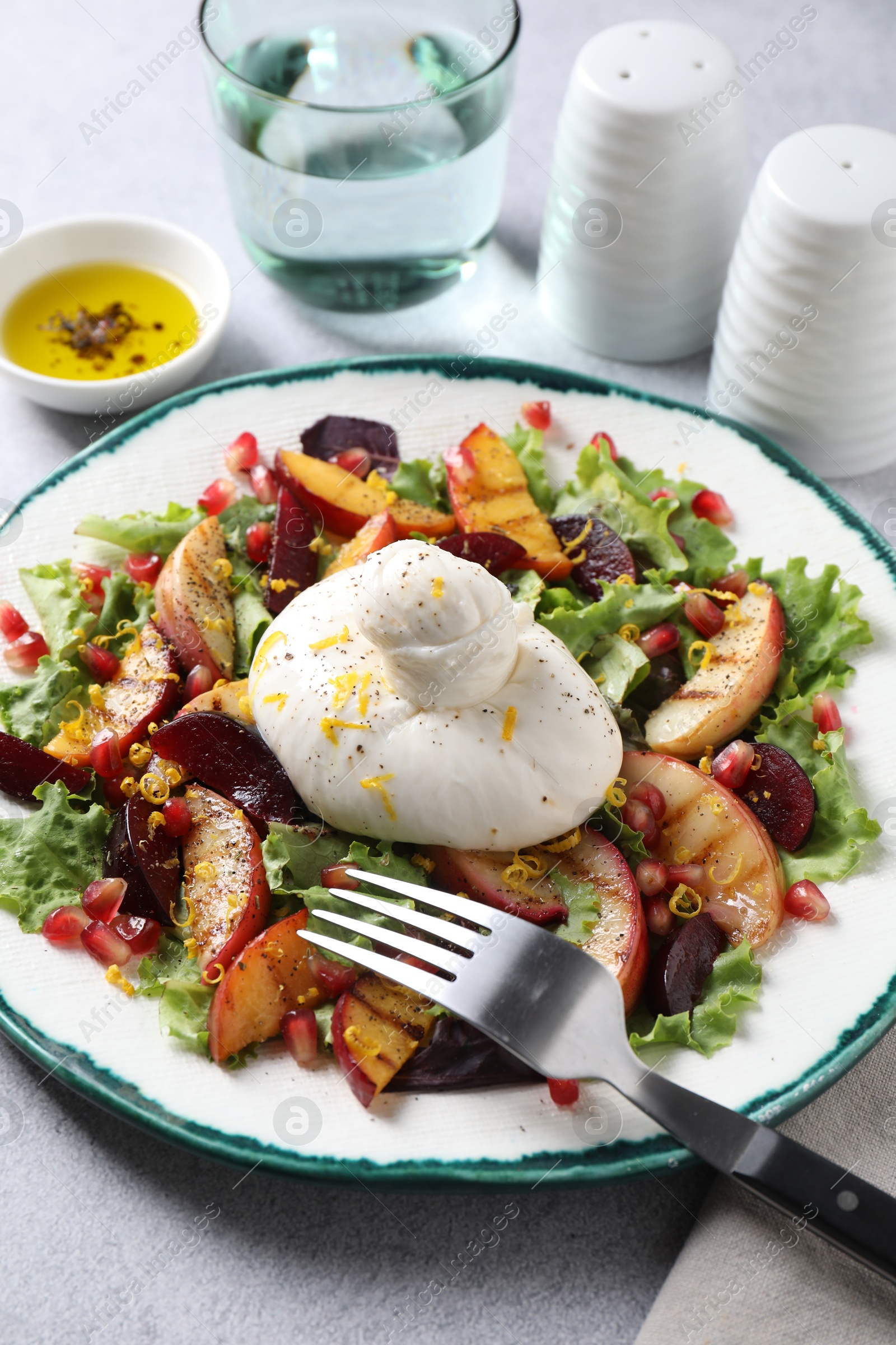 Photo of Plate with fresh burrata salad on grey textured table, closeup