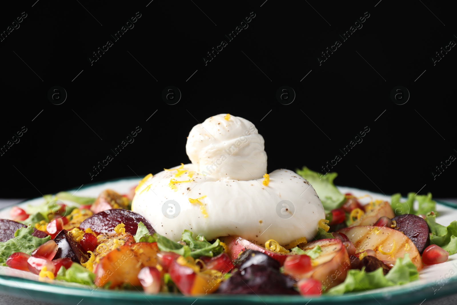 Photo of Plate with fresh burrata salad on plate against black background, closeup