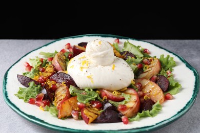 Photo of Plate with fresh burrata salad on grey table against black background, closeup