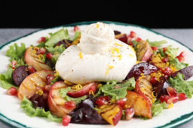 Plate with fresh burrata salad on grey table against black background, closeup