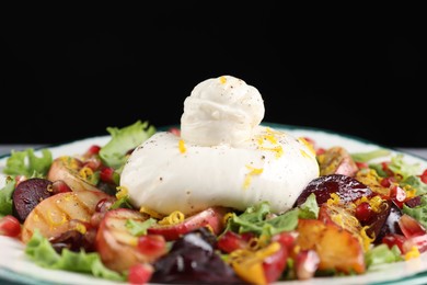 Photo of Fresh burrata salad on plate against black background, closeup