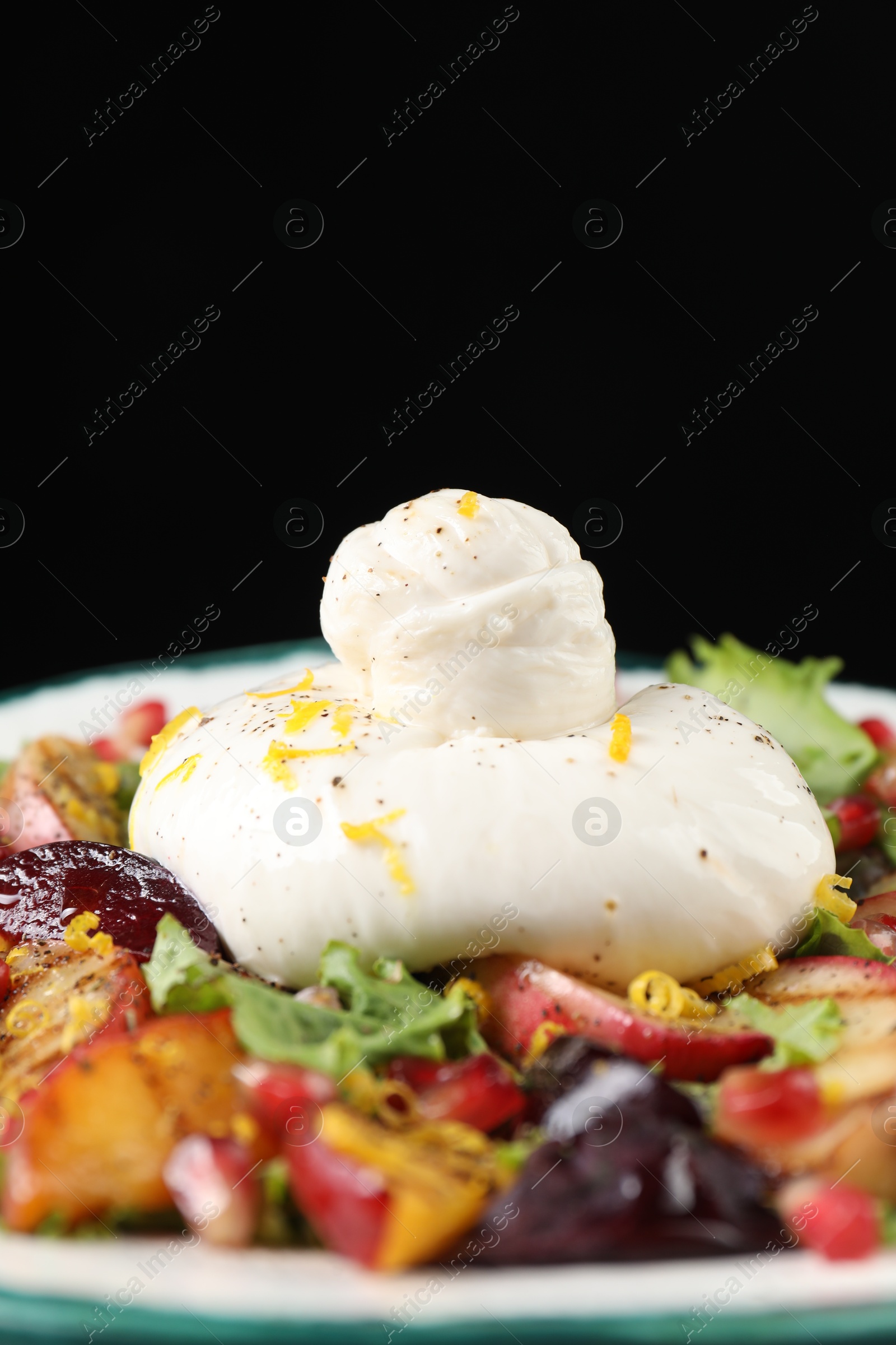 Photo of Plate with fresh burrata salad on plate against black background, closeup