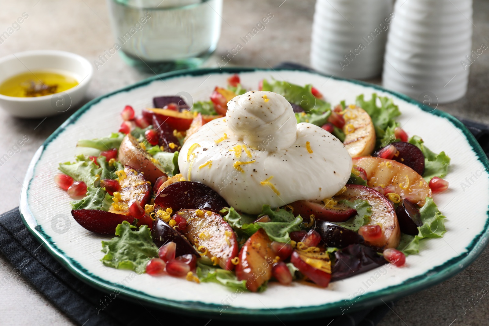 Photo of Plate with fresh burrata salad on grey textured table, closeup