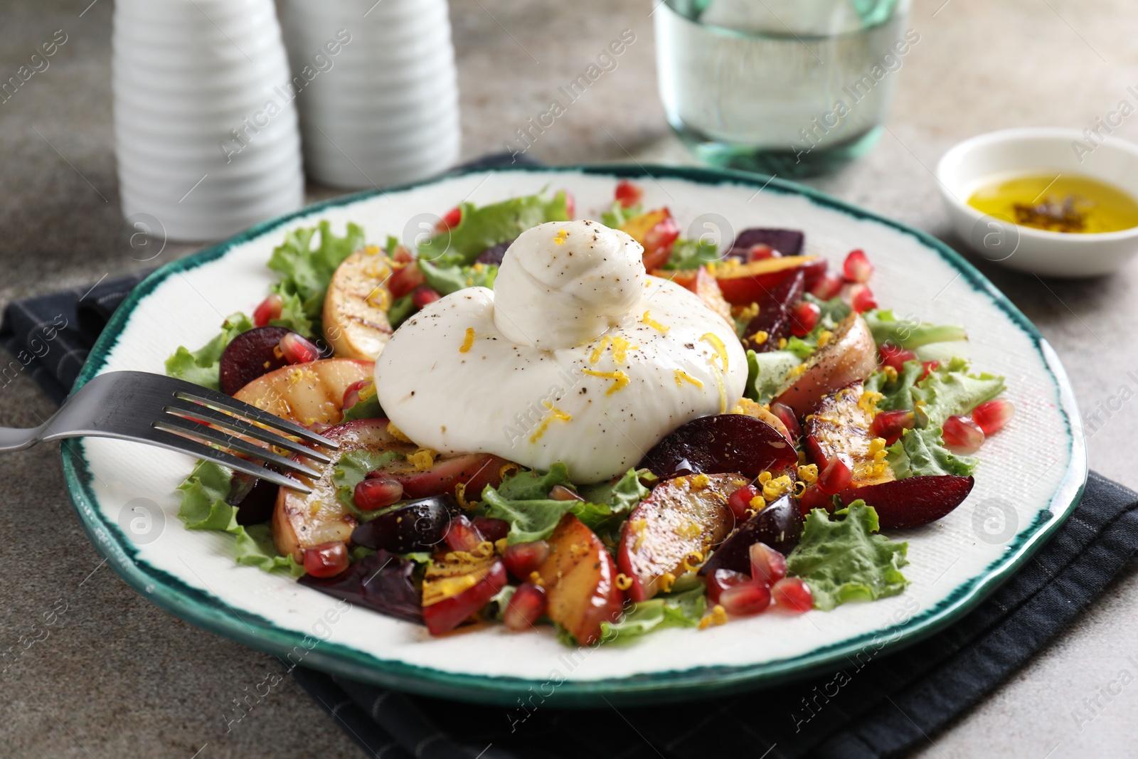 Photo of Plate with fresh burrata salad on grey textured table, closeup