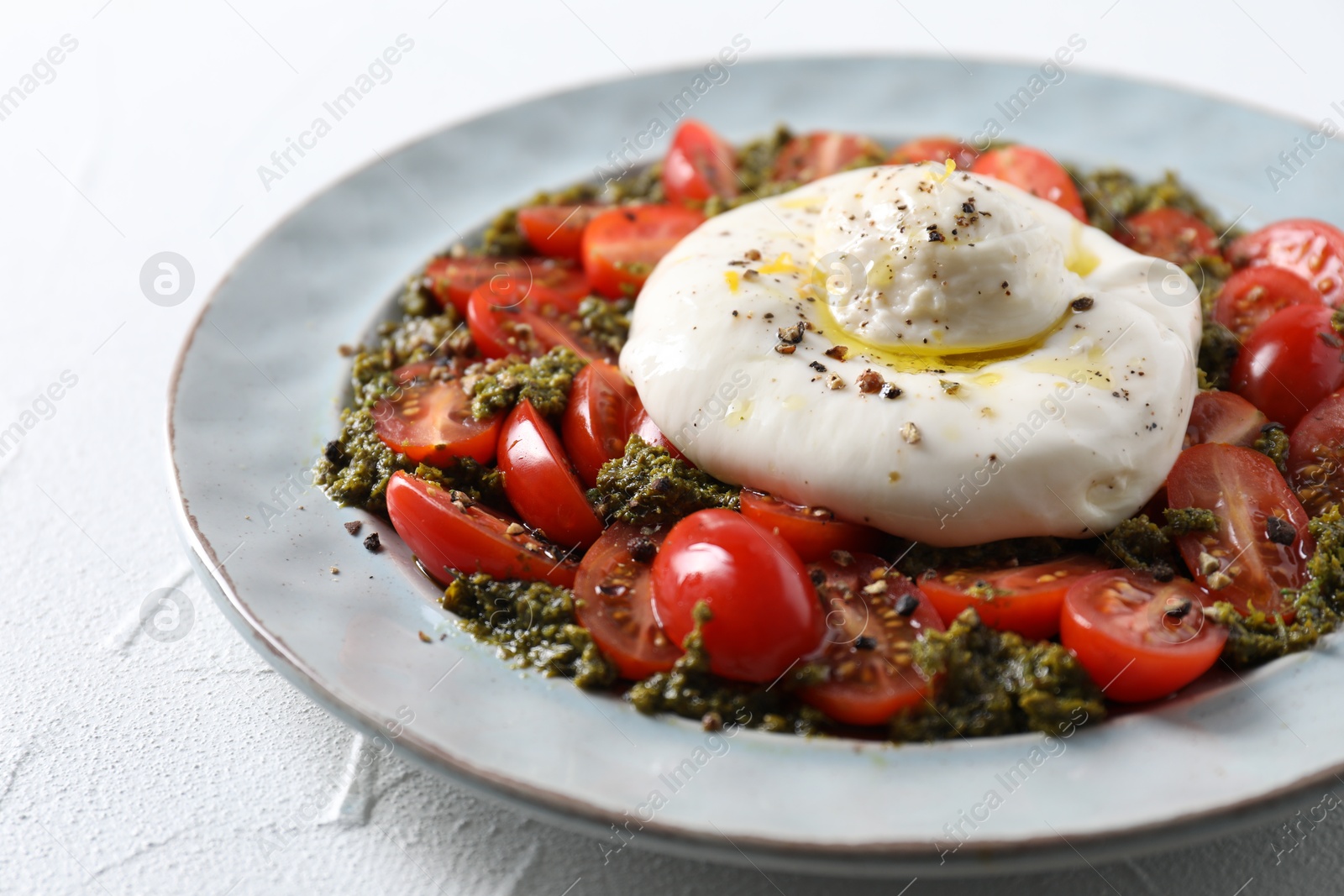 Photo of Fresh delicious burrata salad on white table, closeup