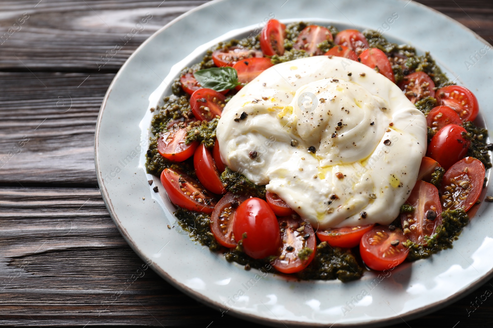 Photo of Fresh delicious burrata salad on wooden table, closeup