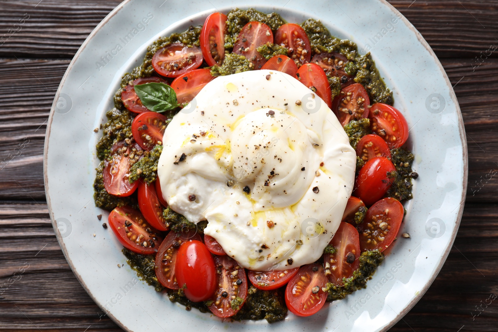 Photo of Fresh delicious burrata salad on wooden table, top view