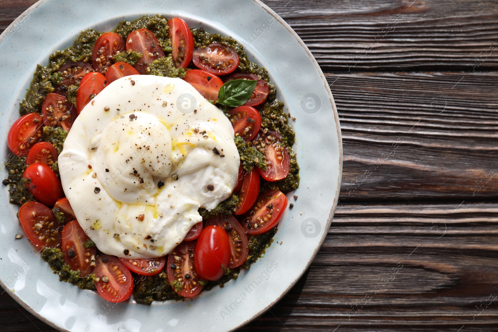 Photo of Fresh delicious burrata salad on wooden table, top view. Space for text