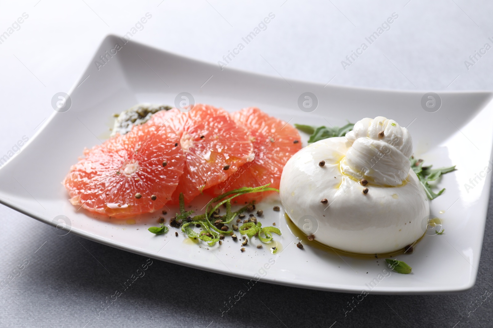 Photo of Delicious burrata cheese, grapefruit and spices on light grey table, closeup