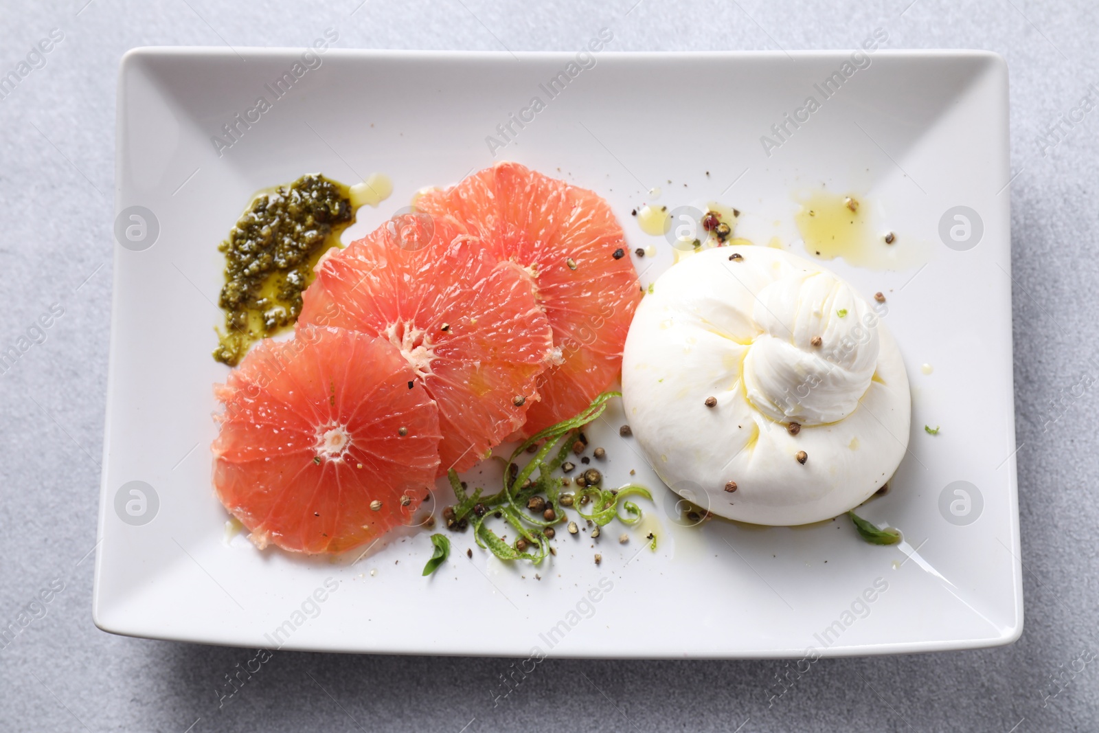 Photo of Delicious burrata cheese, grapefruit and spices on light grey table, top view