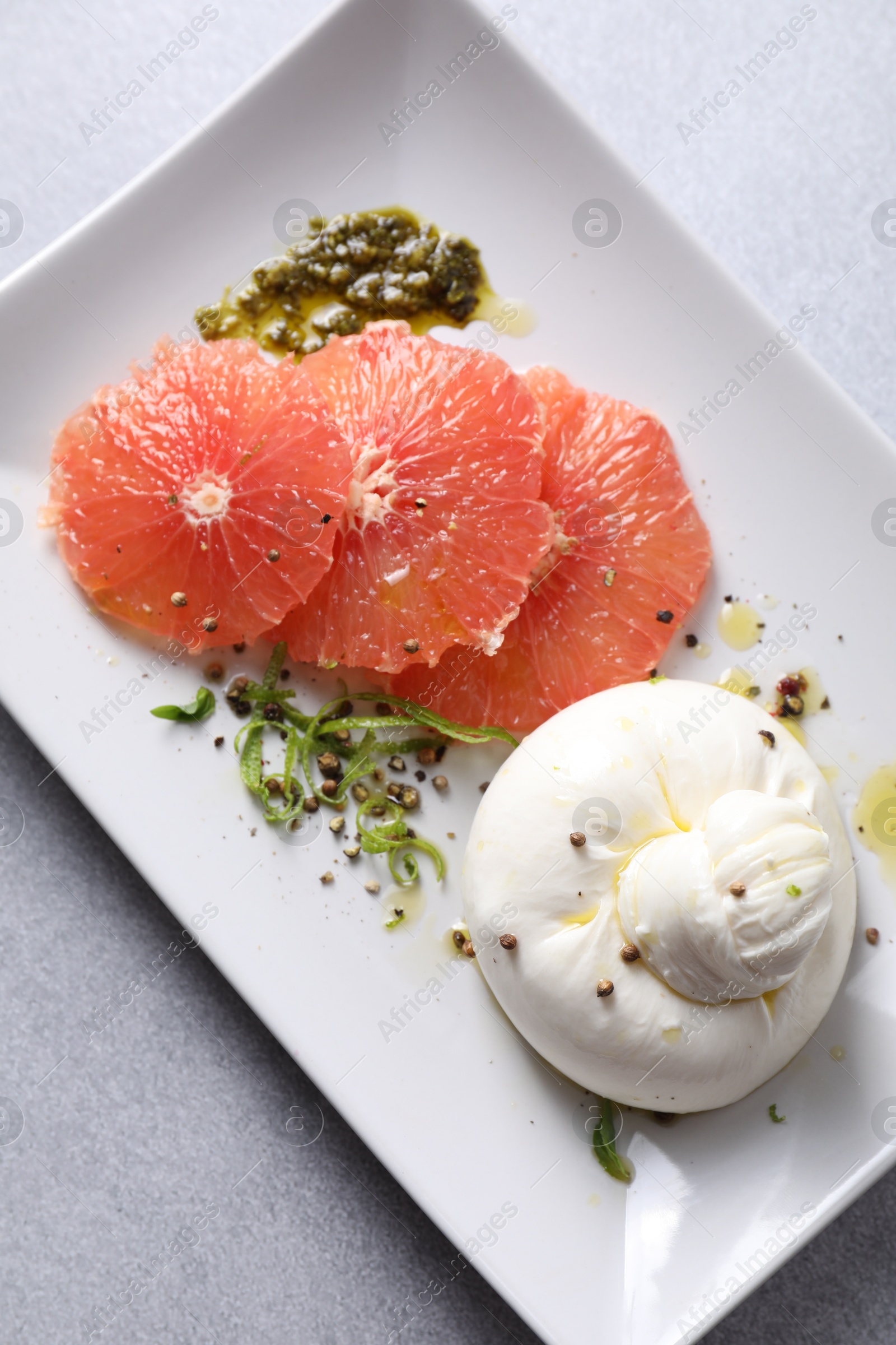 Photo of Delicious burrata cheese, grapefruit and spices on light grey table, top view