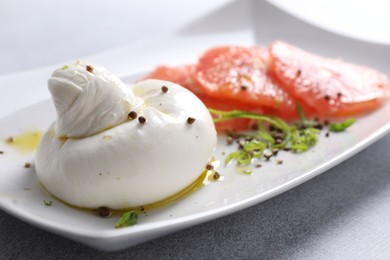 Delicious burrata cheese, grapefruit and spices on light grey table, closeup