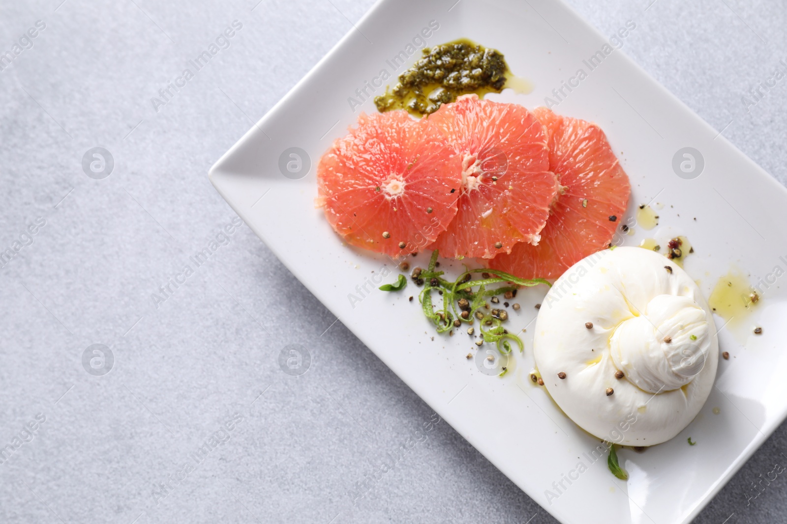 Photo of Delicious burrata cheese, grapefruit and spices on light grey table, top view. Space for text