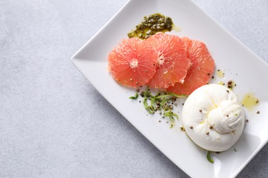 Delicious burrata cheese, grapefruit and spices on light grey table, top view. Space for text