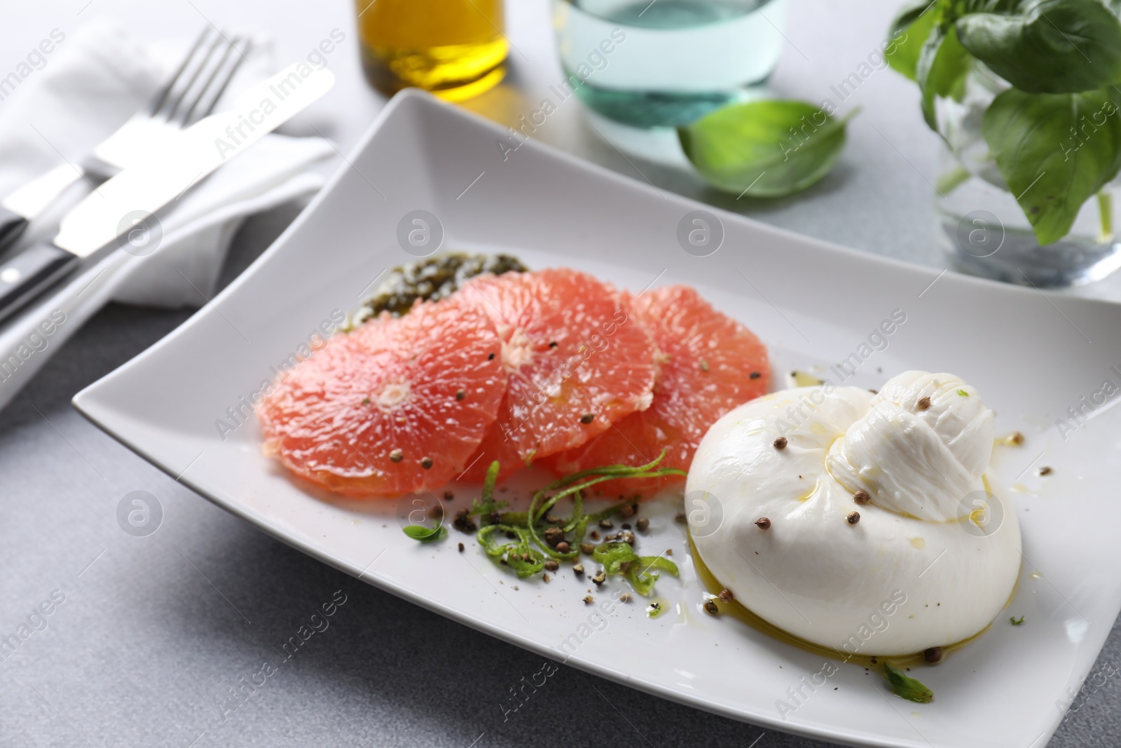 Photo of Delicious burrata cheese, grapefruit and spices on light grey table, closeup