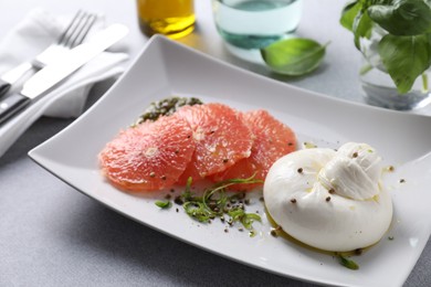 Delicious burrata cheese, grapefruit and spices on light grey table, closeup