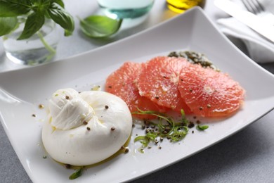 Photo of Delicious burrata cheese, grapefruit and spices on light grey table, closeup