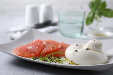 Photo of Delicious burrata cheese, grapefruit and spices on light grey table, closeup