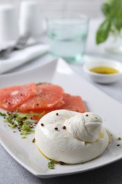 Photo of Delicious burrata cheese, grapefruit and spices on light grey table, closeup