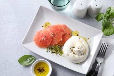 Delicious burrata cheese and grapefruit served on light grey table, top view