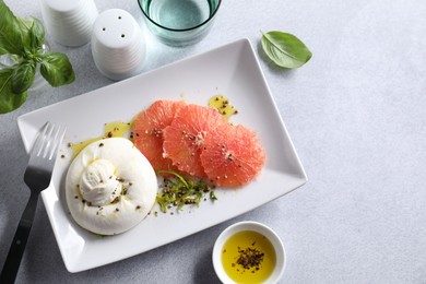 Photo of Delicious burrata cheese and grapefruit served on light grey table, top view