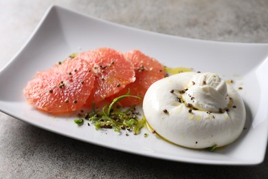 Delicious burrata cheese, grapefruit and spices on grey table, closeup