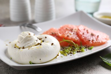 Photo of Delicious burrata cheese, grapefruit and spices on grey table, closeup